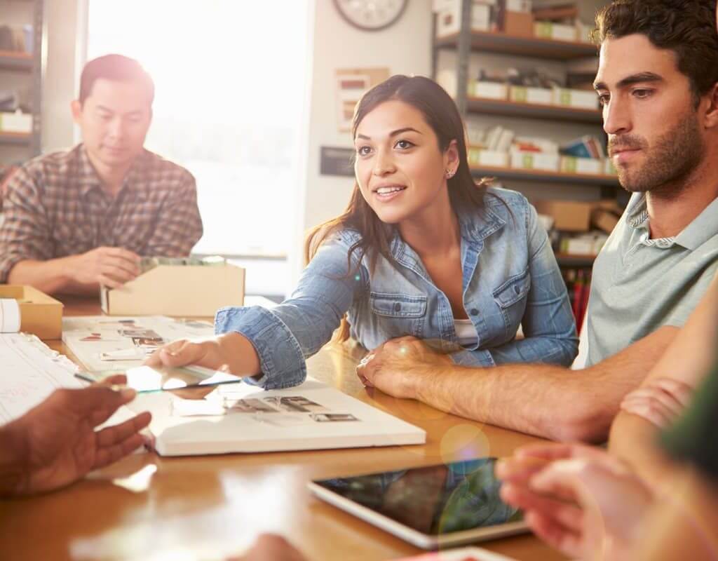 The Startup Working Environment – a Challenging Space or the Space to take on Challenges? image - woman with brown hair sat at a table discusses a creative project with three male colleagues