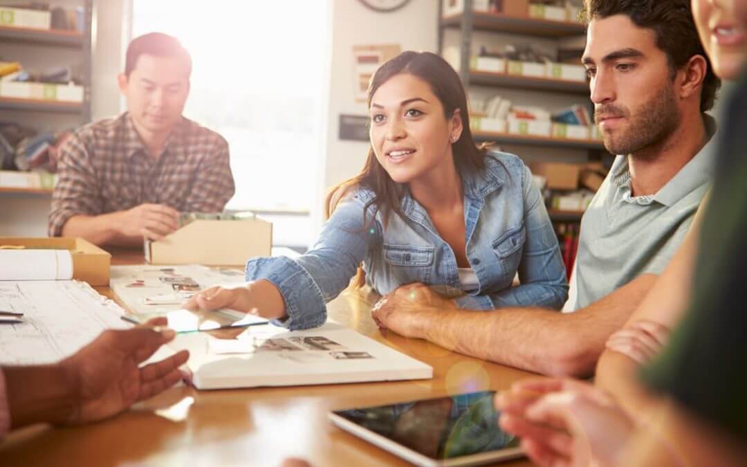 The Startup Working Environment – a Challenging Space or the Space to take on Challenges? image - woman with brown hair sat at a table discusses a creative project with three male colleagues