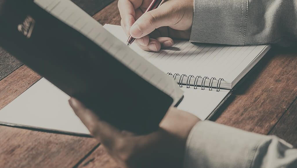 The Ultimate Start-up Checklist image - man's arms writing in a notebook on a wooden desk