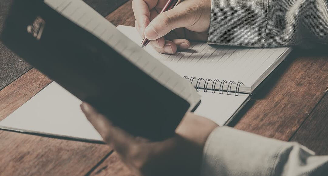 The Ultimate Start-up Checklist image - man's arms writing in a notebook on a wooden desk