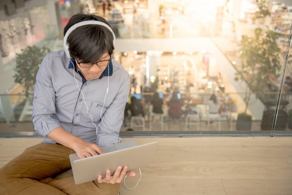 Image - young man sitting on floor in a co-working space using laptop and headphones