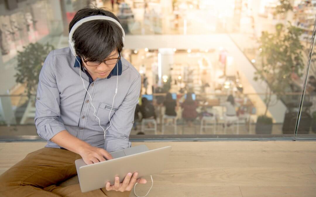 Image - young man sitting on floor in a co-working space using laptop and headphones