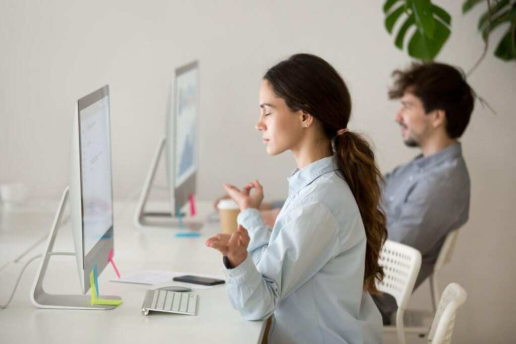 Image - female office worker meditating at her desk in front of computer, hands pressed together