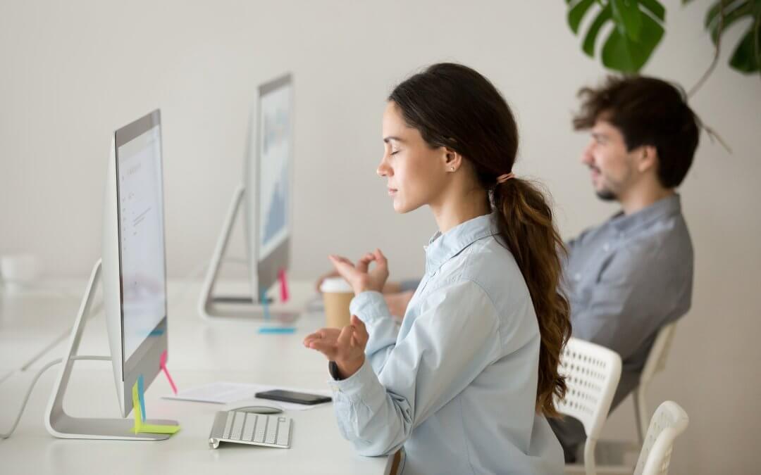 Image - female office worker meditating at her desk in front of computer, hands pressed together