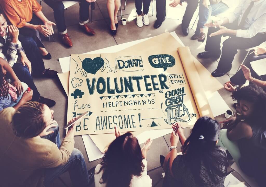 Image - people gathered in a circle, poster with charity and volunteering slogans and motivational quotes written on it in middle of circle