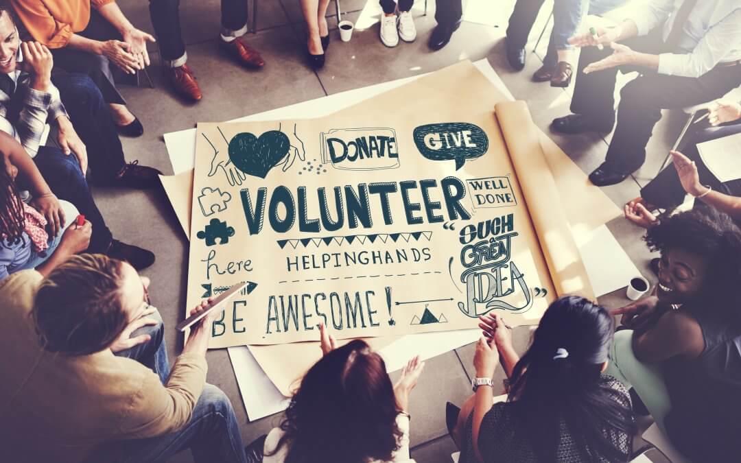 Image - people gathered in a circle, poster with charity and volunteering slogans and motivational quotes written on it in middle of circle