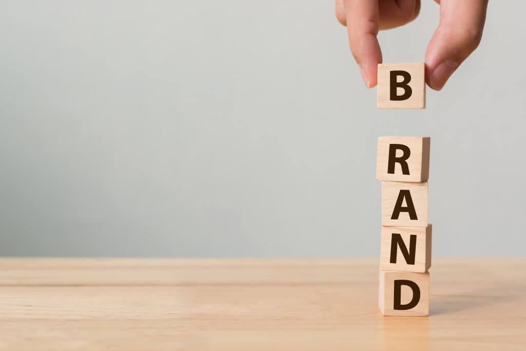 Image - hand putting final "B" block on top of pile of lettered blocks spelling "branding", on wooden table