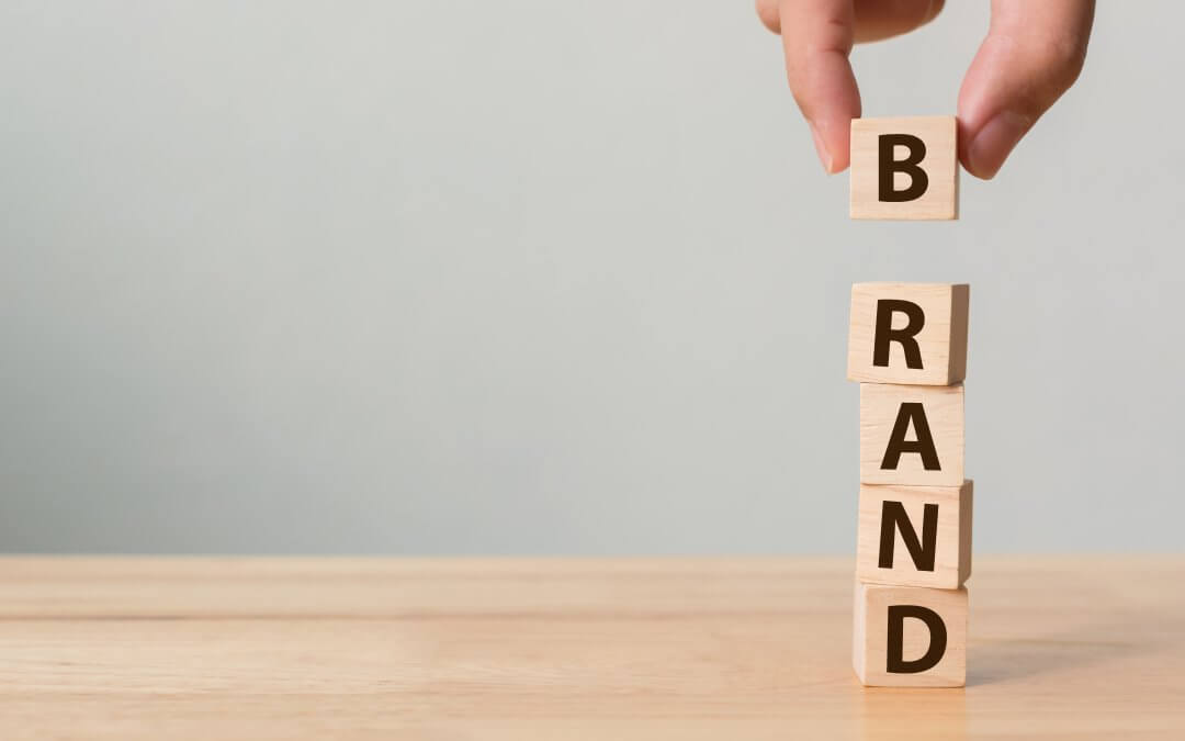 Image - hand putting final "B" block on top of pile of lettered blocks spelling "branding", on wooden table