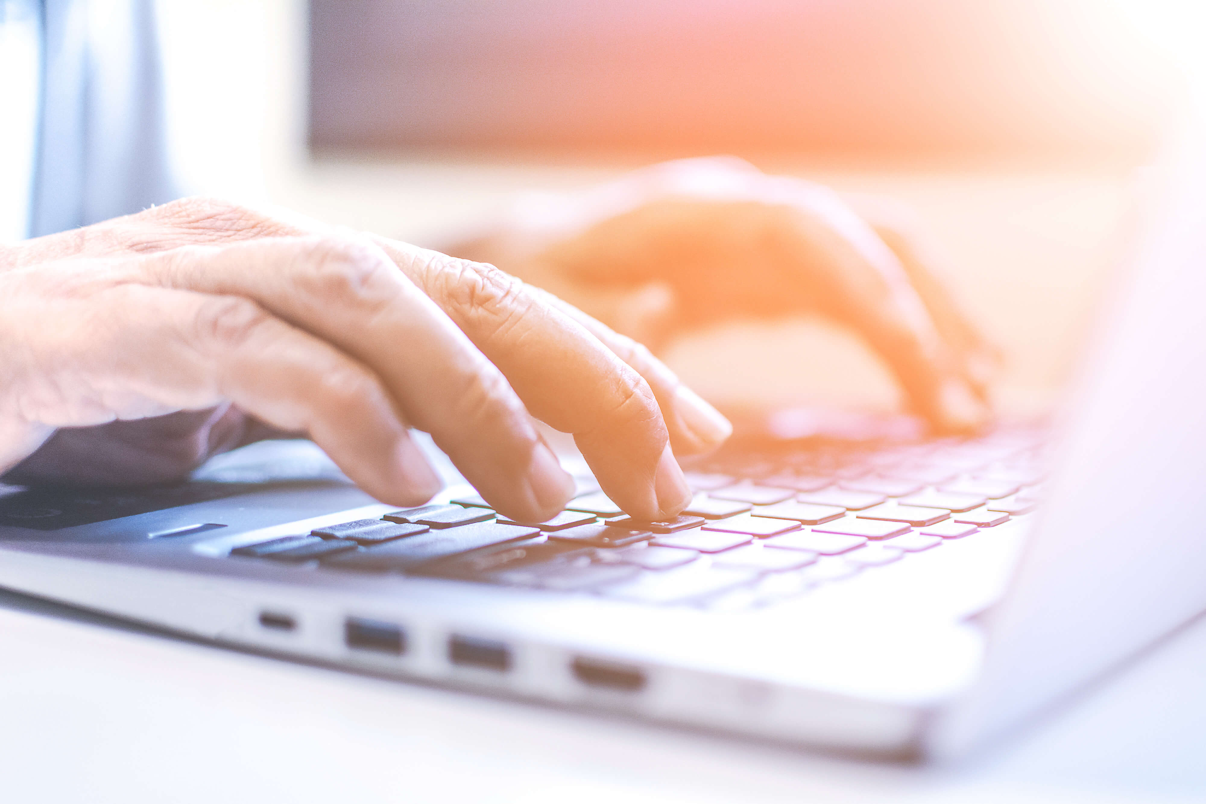 Image - hands typing on laptop, with a sun glare overlay